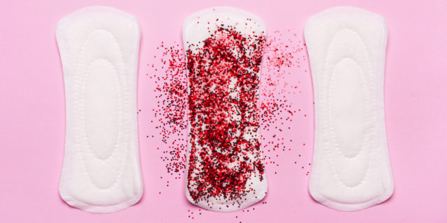 Three pads in a row. The middle one is covered in red glitter, representing period blood
