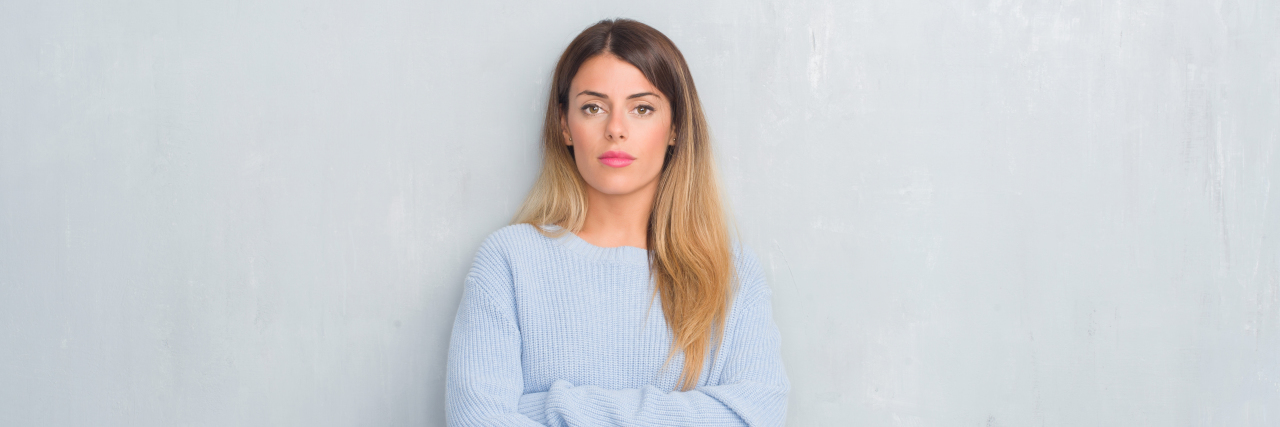 woman in an oversized blue sweater with her arms crossed looking seriously into the camera