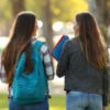 Back view of two happy students walking and talking in a university campus