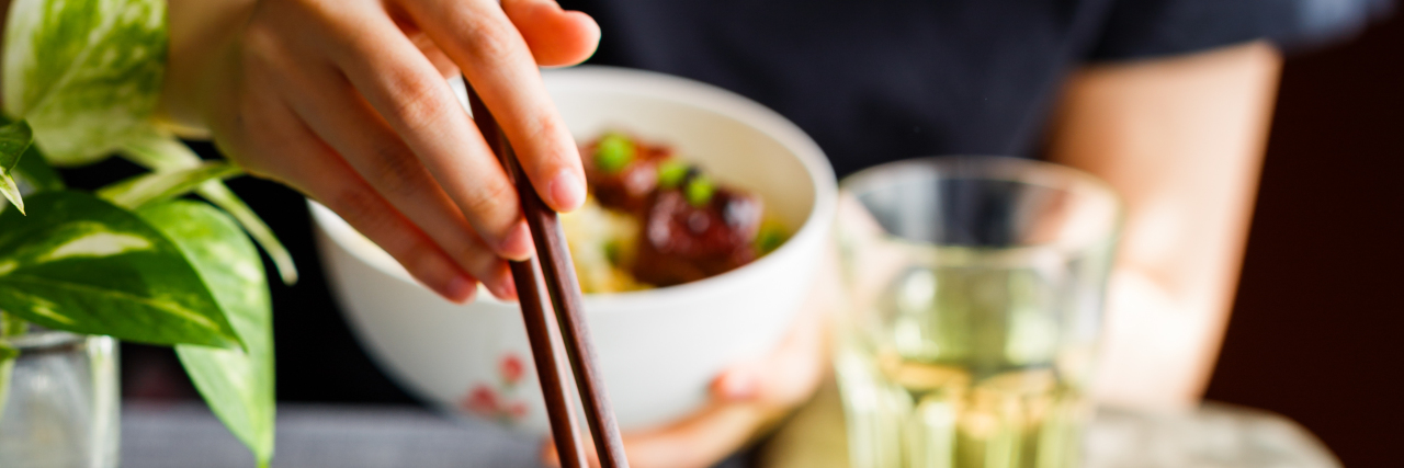 My Eating Disorder Cared More About Food Than My Grandpa's Death photo of woman picking up chinese food with chopsticks while holding her own bowl