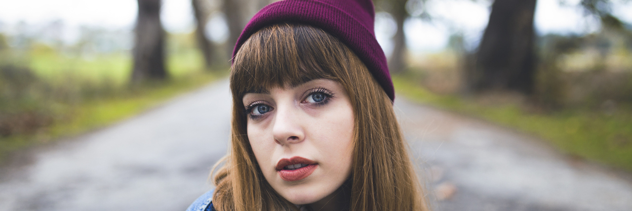 When the System Fails You as Someone With Bipolar Disorder Young woman with long brown hair and bangs, standing outside on a path and looking at the camera