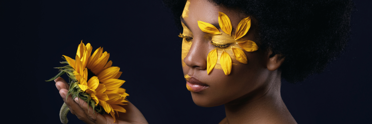 African-American woman with a sunflower and creative makeup on her face.