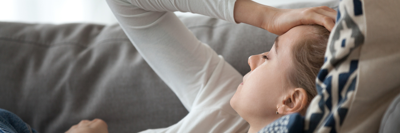My Family Struggles to Accept My Chronic Illness Woman lying on the couch with a headache.