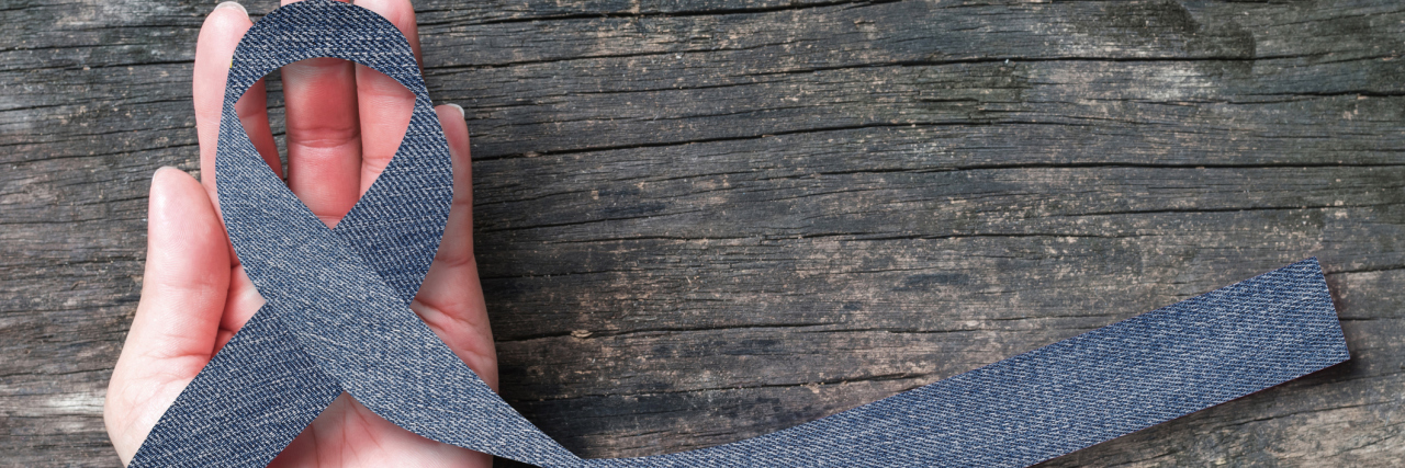 Why Rare Disease Day Means so Much to Me Woman's hand holding a blue denim ribbon for rare disease awareness.