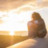 a woman with curly hair is sitting outside on a wall enjoying the sunset