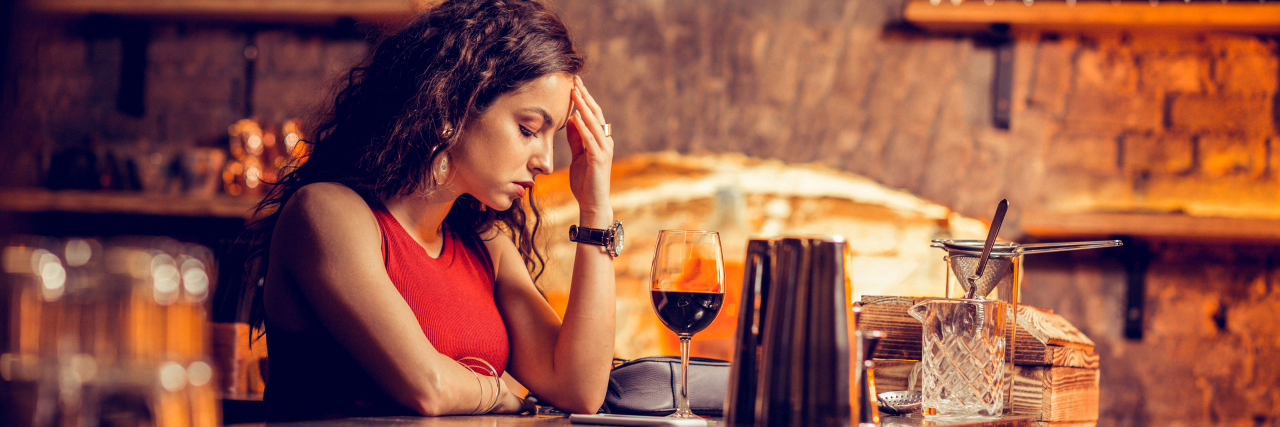 What My Anxiety Sounds Like on a Night Out in Public woman in a red dress sitting at bar with her head down