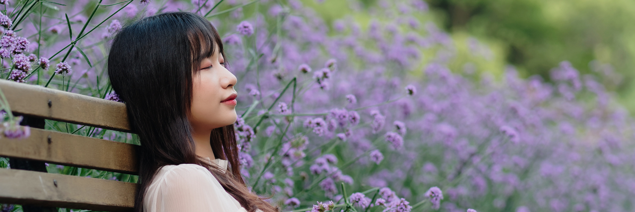 Being Busy Is Not as Important as Taking Time for Your Mental Health Woman sitting on a bench near some purple flowers