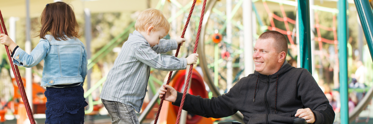 Teaching the Next Generation About Disability Man in wheelchair plays with kids on the playground.