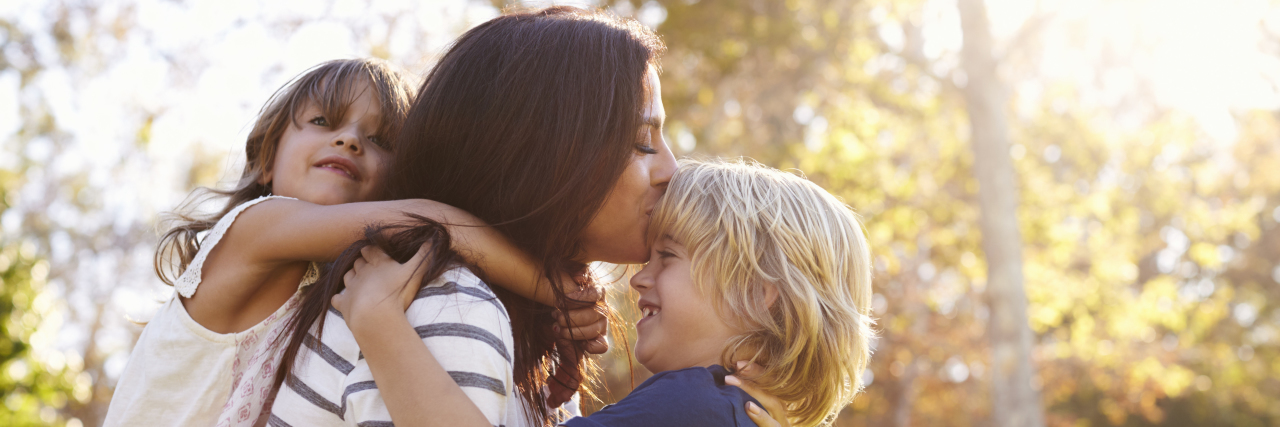 What a Day in the Life of a Mom's Battle With Depression Looks Like mother holding son kissing his forehead with her daughter on her back holding onto her