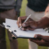 cropped view of african american man writing something on paper in clipboard