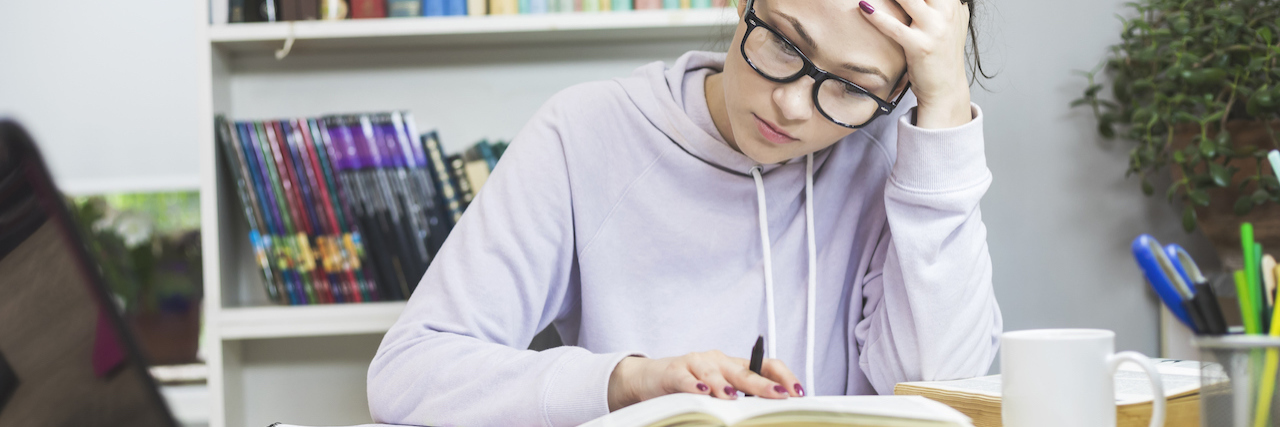 Inside the Mind of an AP Student With Mental Illness Student sitting at desk with computer and books, holding her head in her hand