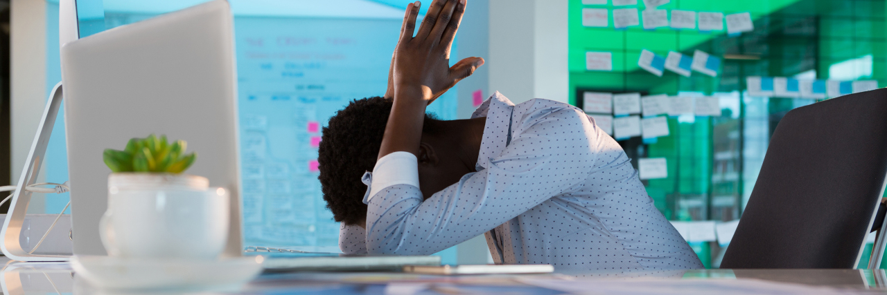How Technology and Online Communication Increase Cyberstalking Trauma woman sitting at a white desk in front of a computer with her head down in frustration