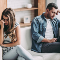 Upset couple at home. Handsome man and beautiful young woman are having quarrel. Sitting on sofa together. Family problems.