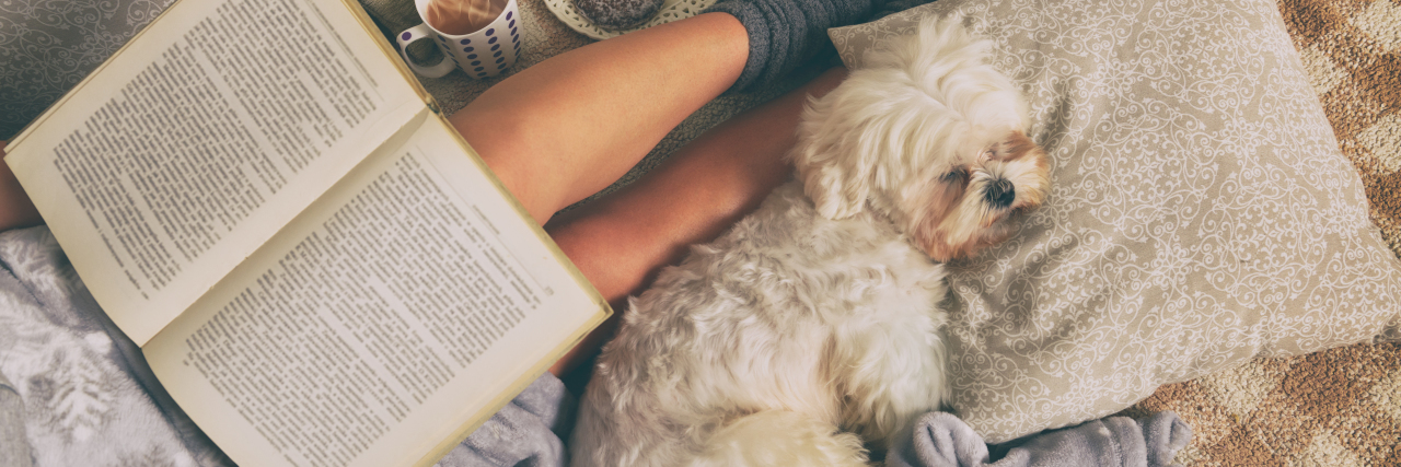 3 Books That Can Help You Manage Chronic Pain Woman lying on bed with dog reading a book.
