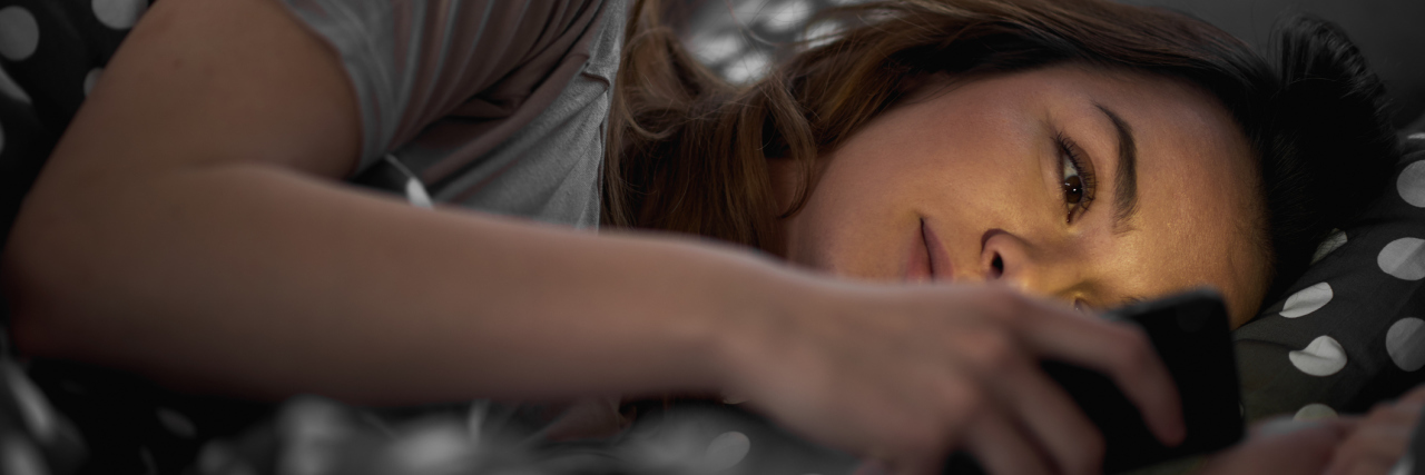 Woman using smart phone and lying down in bed late at night
