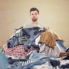 man buried in a heap of laundry with a confused look on his face