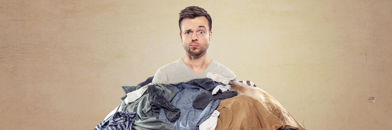 3 Simple Ways to Clean and Declutter That Can Help Depression man buried in a heap of laundry with a confused look on his face