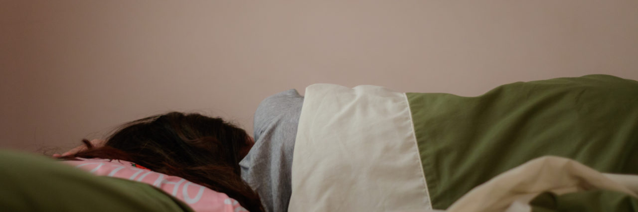 a young woman lying in a bed with face toward the wall