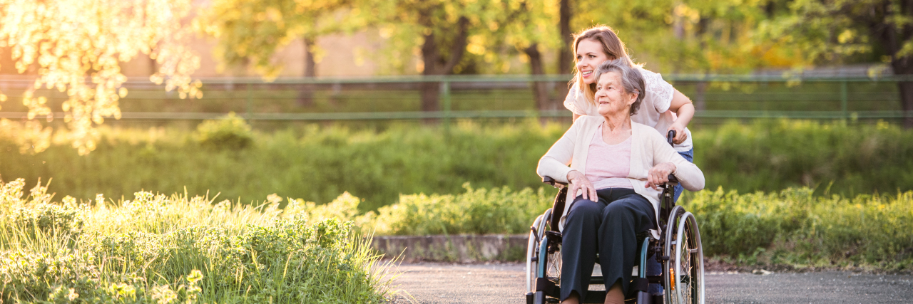 Caregiver pushing elderly woman's wheelchair.
