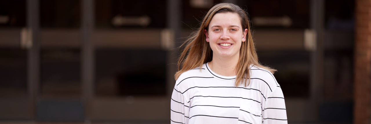 Hannah Neild in a white and black stripped shirt in front of a building