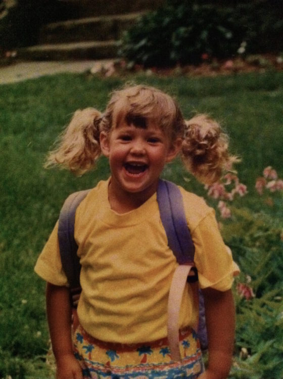 A smiling young girl with pigtails and a backpack