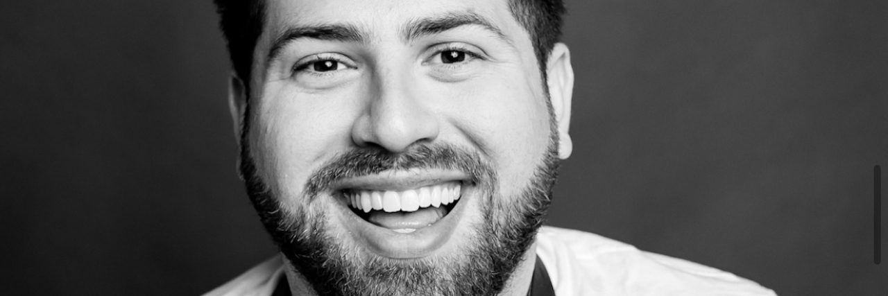 How Common Are Eating Disorders in Men? Black and white portrait of Ryan Sheldon. He’s smiling at the camera and wearing a white v-neck shirt.