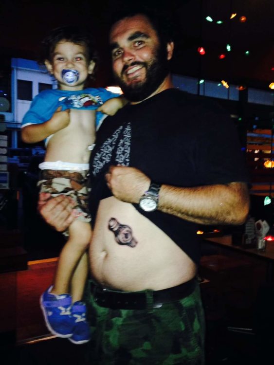 the author's child smiling and showing his feeding tube, and the father holding him up, showing his feeding tube tattoo on his stomach