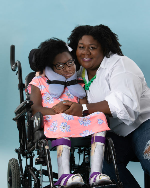 A mother is taking a picture with her daughter who uses a wheelchair.