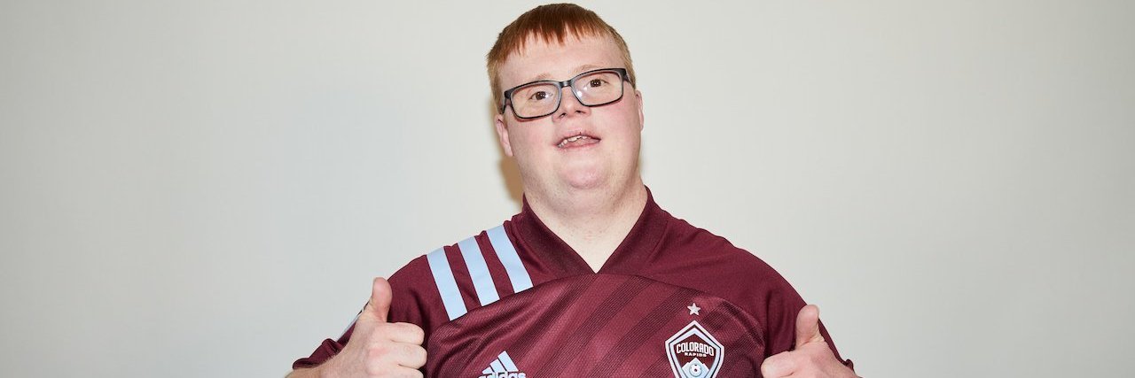 Special Olympian and soccer player Scotty Stephens, a white man with Down syndrome, wearing a maroon jersey and giving two thumbs up