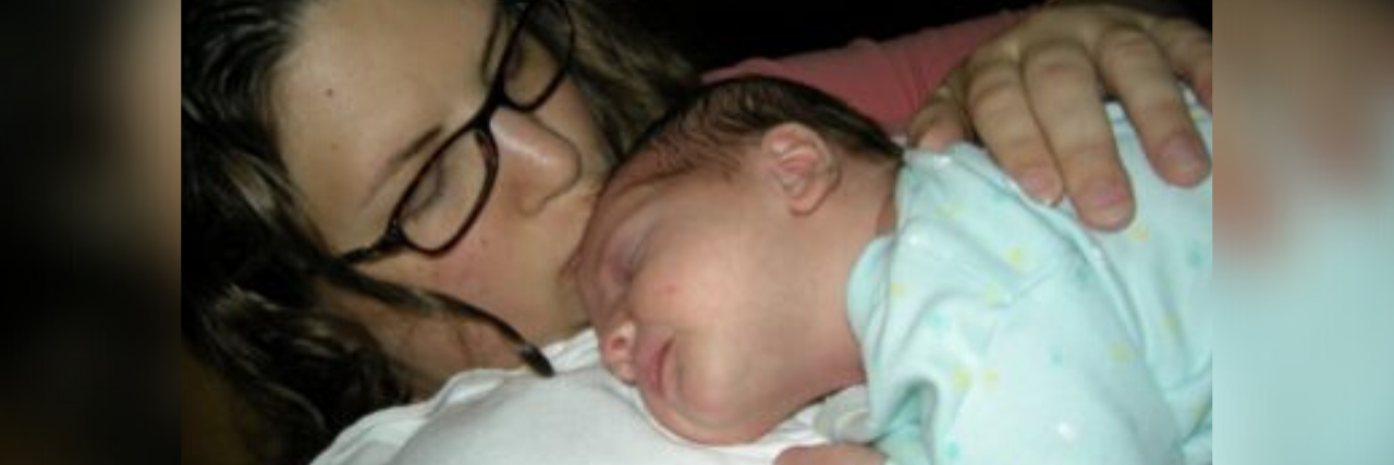 My Traumatic Birthing Experience Didn't Feel 'Bad Enough' to Be Trauma woman (author) kissing the top of her baby's forehead while he's sleeping, holding him