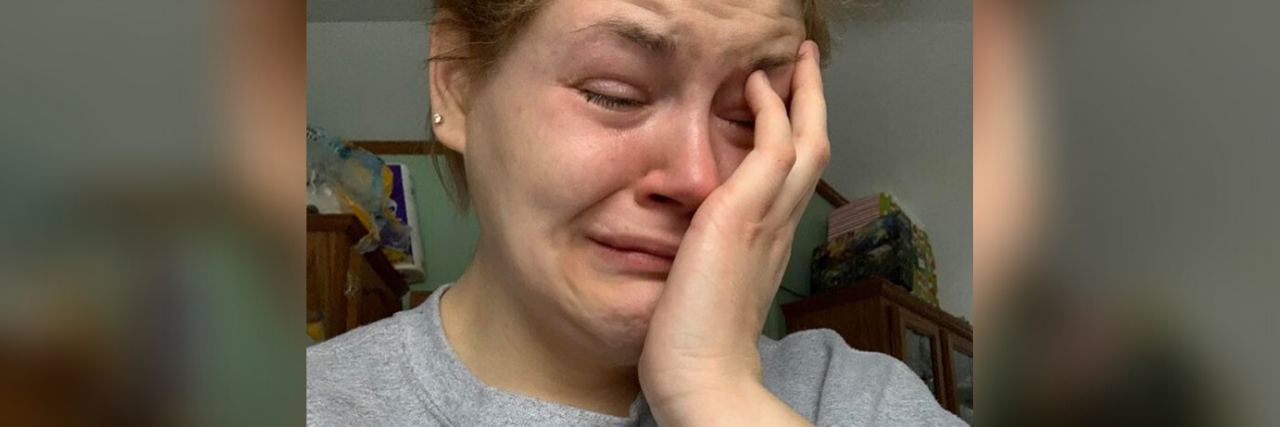 Viral Facebook Post Shows Reality of Being a Stay-at-Home Mom The author crying, wearing a grey t-shirt with her hair pulled back.