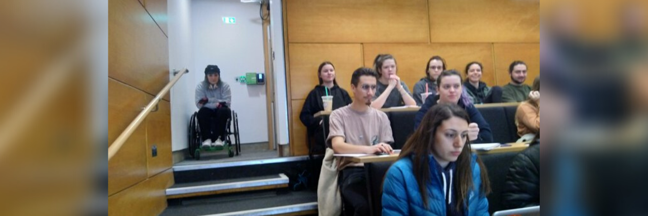Viral Photo on Twitter Shows How Inaccessible College Campuses Can Be Woman in a wheelchair sitting at the top of the steps in a classroom that is not accessible for her