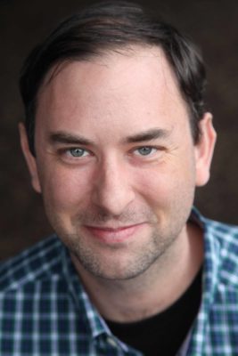 photo of author in a collared checkered blue shirt smiling 