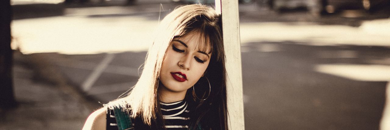 What I Mean When I Say 'I'm Fine' as I Struggle With Mental Illness woman in a striped shirt and overalls leaning against a pole outside with her eyes closed