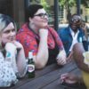 photo of several plus-size people of different ethnicities sitting at table talking and drinking beer
