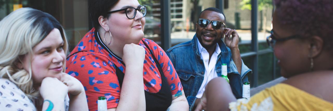 photo of several plus-size people of different ethnicities sitting at table talking and drinking beer