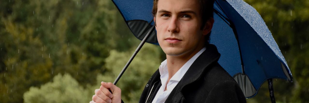 photo of man with blue umbrella looking into camera with serious expression