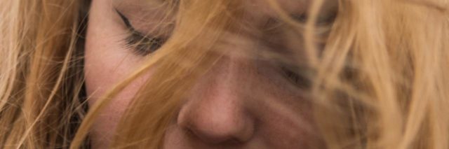 Close-up of a woman's face, eyes closed and hair blowing in wind.