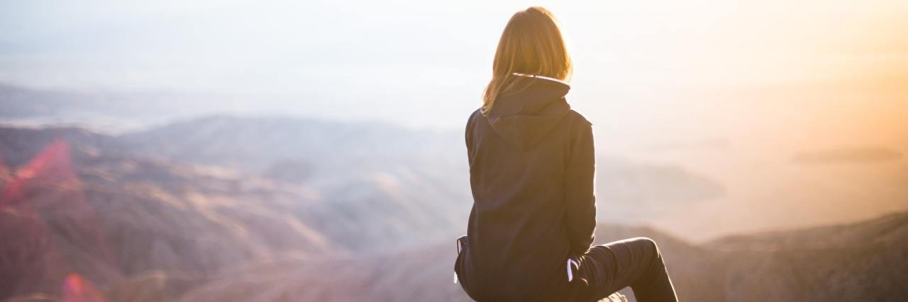 Woman watching the sunset from the top of a mountain.