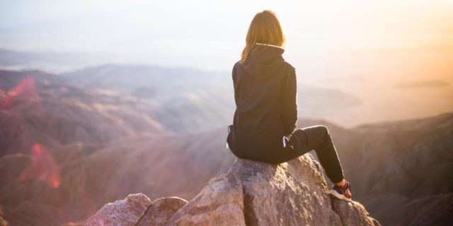 Woman watching the sunset from the top of a mountain.