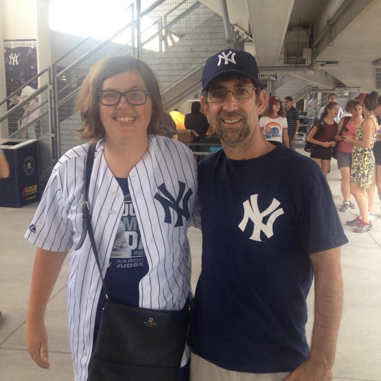 a young woman and a man at a sporting event in Yankees gear posing for a picture