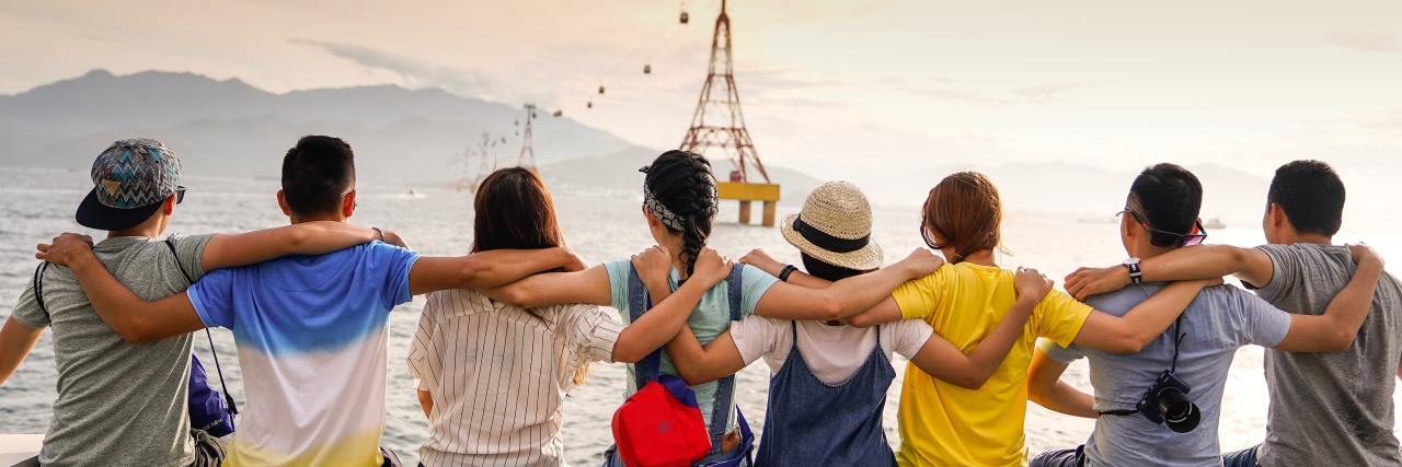 The Power Kindness Can Have in the Depths of Depression group of friends with their arms around each other sitting on a ledge overlooking the mountains