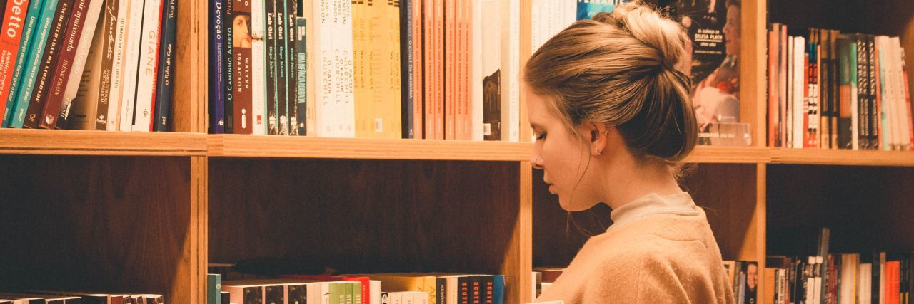 girl with her hair in a bun at a library choosing a book from the bookshelf