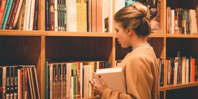 girl with her hair in a bun at a library choosing a book from the bookshelf