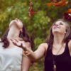 photo of two young women throwing autumn/fall leaves into the air and smiling