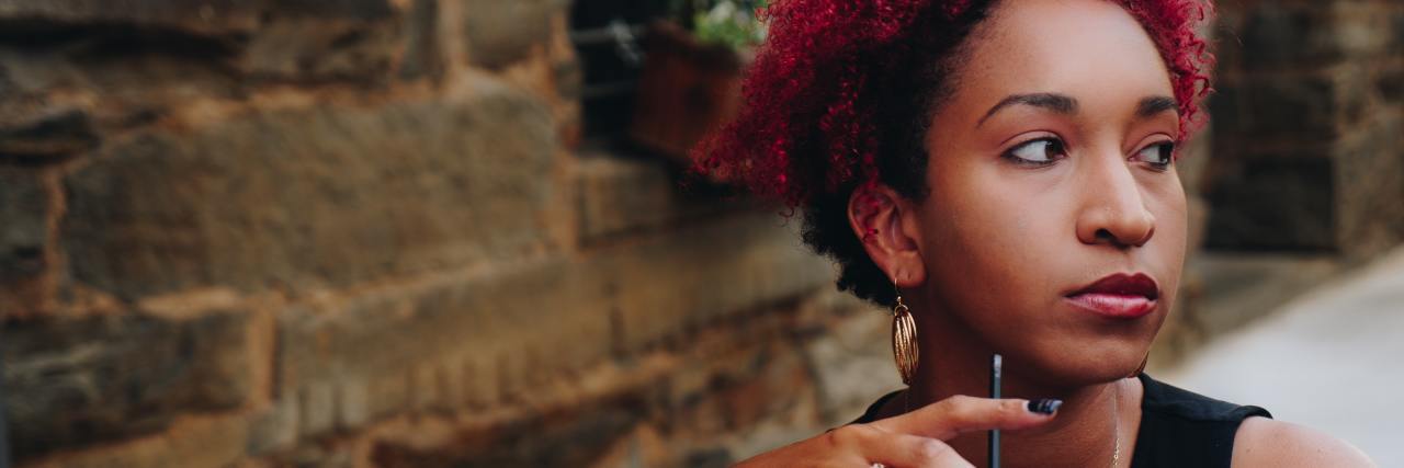 Stop Saying People With Mental Illness Need to 'Get a Thicker Skin' woman with short red hair sitting outside with a cup of iced coffee in her hand