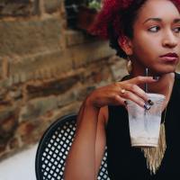 woman with short red hair sitting outside with a cup of iced coffee in her hand