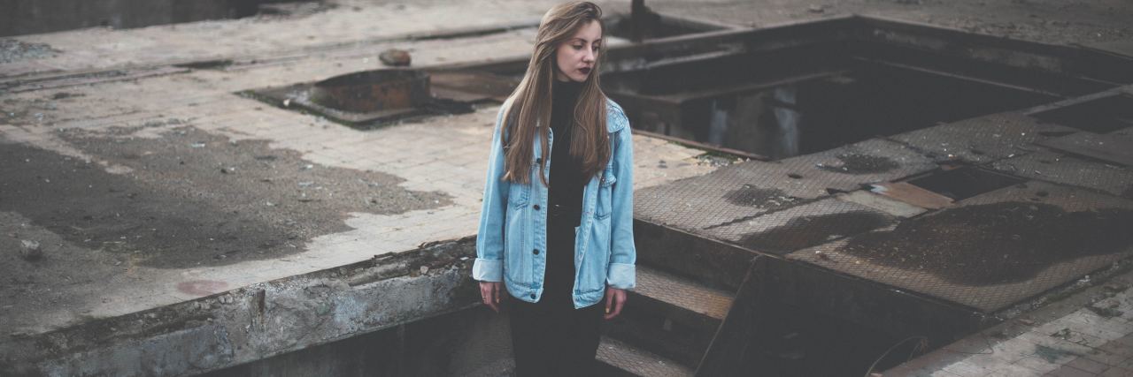 What It Means When People Call You 'Sensitive' photo of blonde woman standing in industrial area with metal stairs, looking sad or thoughtful