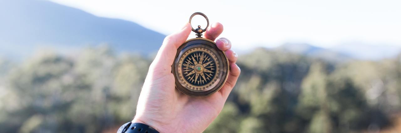 photo of person's hand holding out compass in dusty blurred landscape