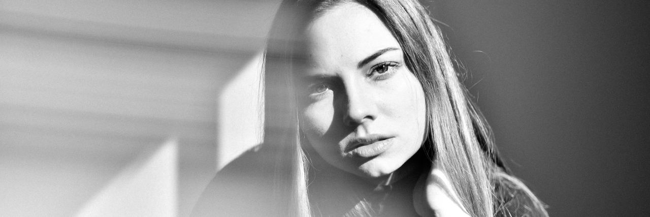 What I Wish I Knew Before Starting My Mental Health Recovery black and white photo of woman with hand to the back of her neck under her hair, looking serious into camera with shafts of light falling across her